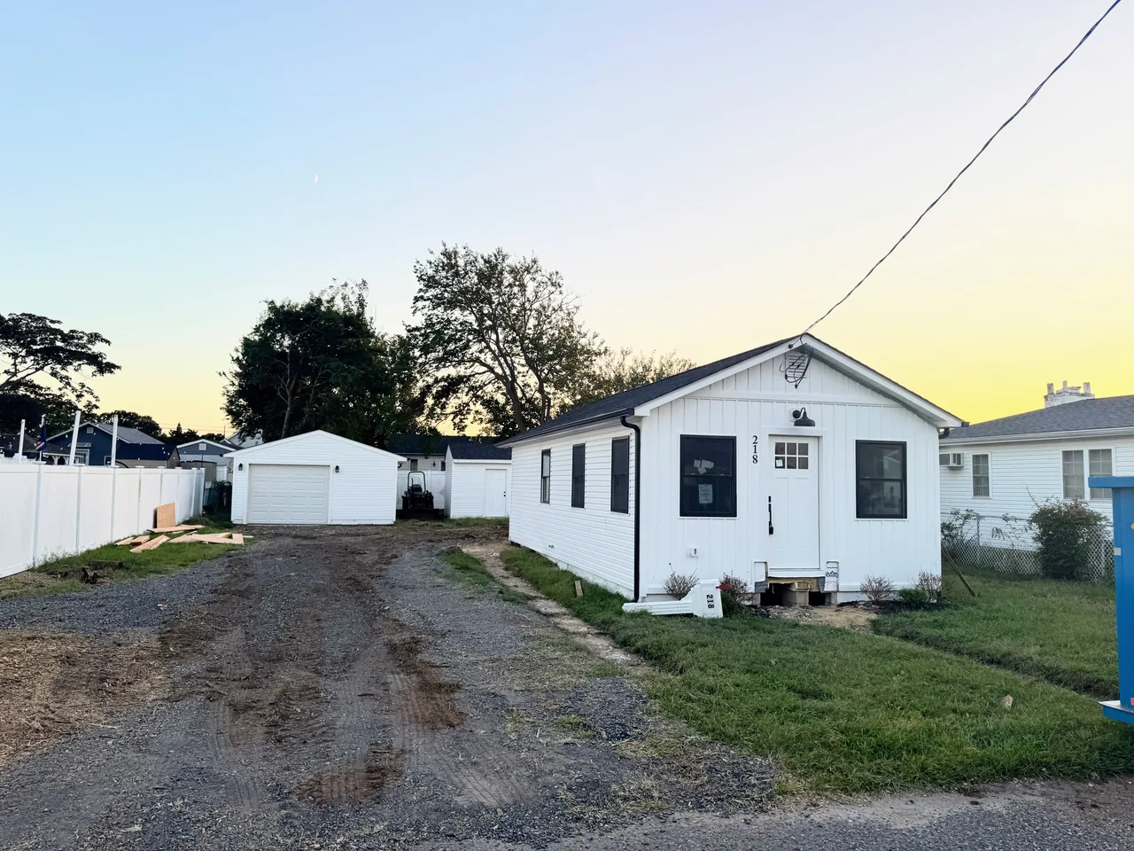 The white Clubhouse cottage and detached garage before renovation, beside an unfinished driveway.